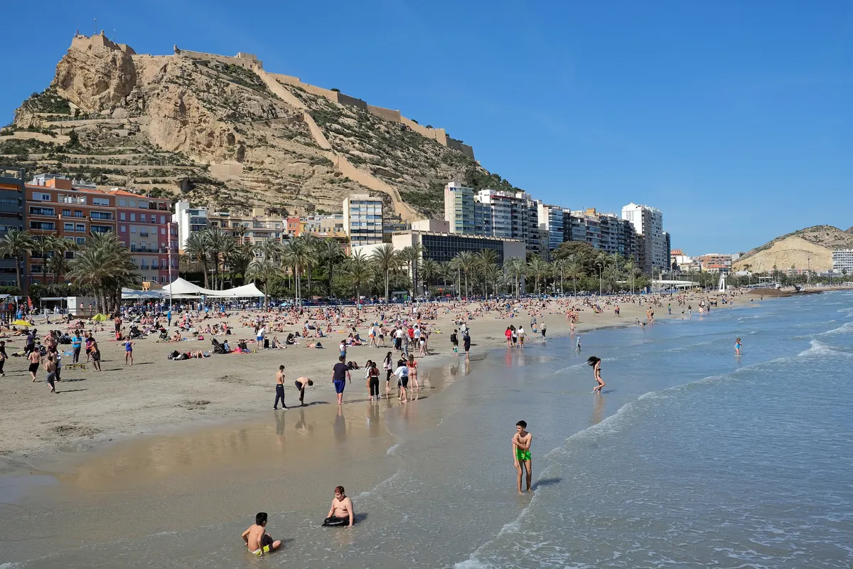 Hrad Santa Bárbara na skalnatém vrchu nad pláží Postiguet v Alicante, s plavci na okraji moře