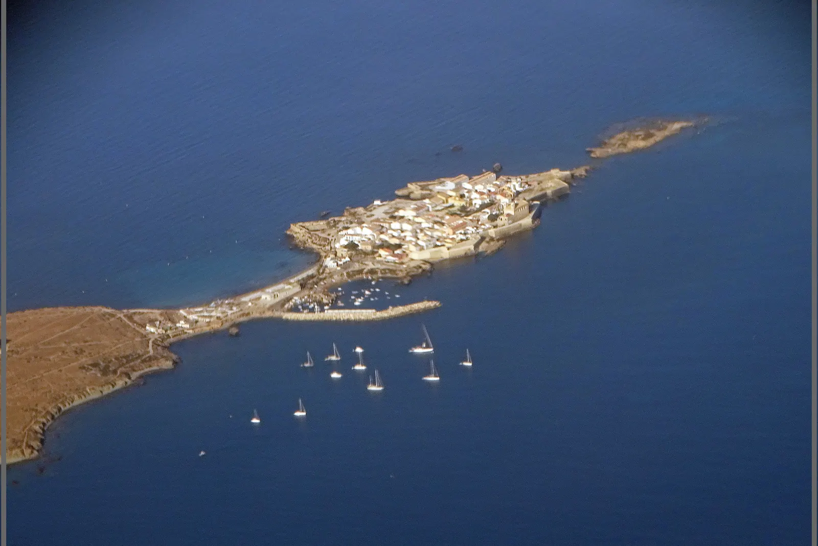 Een luchtfoto van het lage, vlakke eiland Tabarca voor de kust van Alicante, met een klein ommuurd stadje aan één kant en zeilboten voor anker in het blauwe water